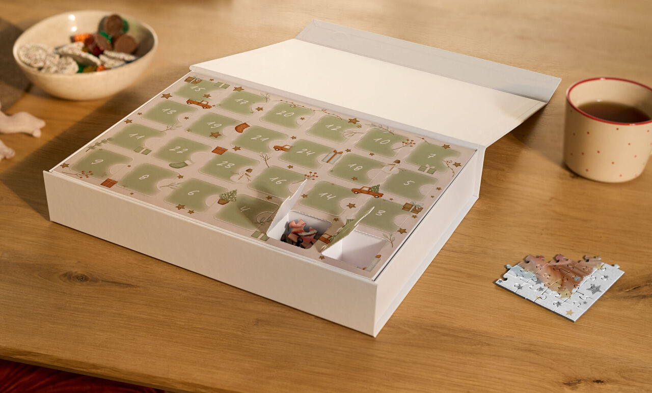 Premium Puzzle-Adventskalender mit zwei geöffneten Türchen und einem bereits gepuzzelten Puzzlestück in weihnachtlicher Umgebung