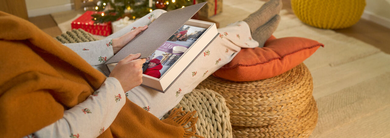 Eine Person öffnet eine Geschenkbox mit einem CEWE FOTOBUCH mit Winterfotos.